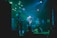 A band is performing on stage with three visible members playing electric guitars under vibrant green and blue stage lights. The atmosphere is energetic, with the audience barely visible in the darker areas, suggesting a lively concert.