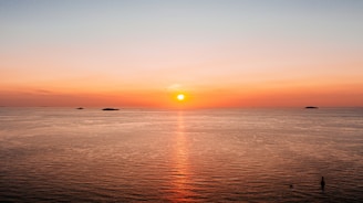 the sun is setting over the ocean with small islands in the distance