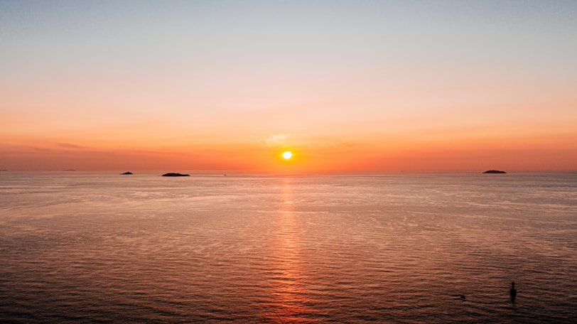 the sun is setting over the ocean with small islands in the distance