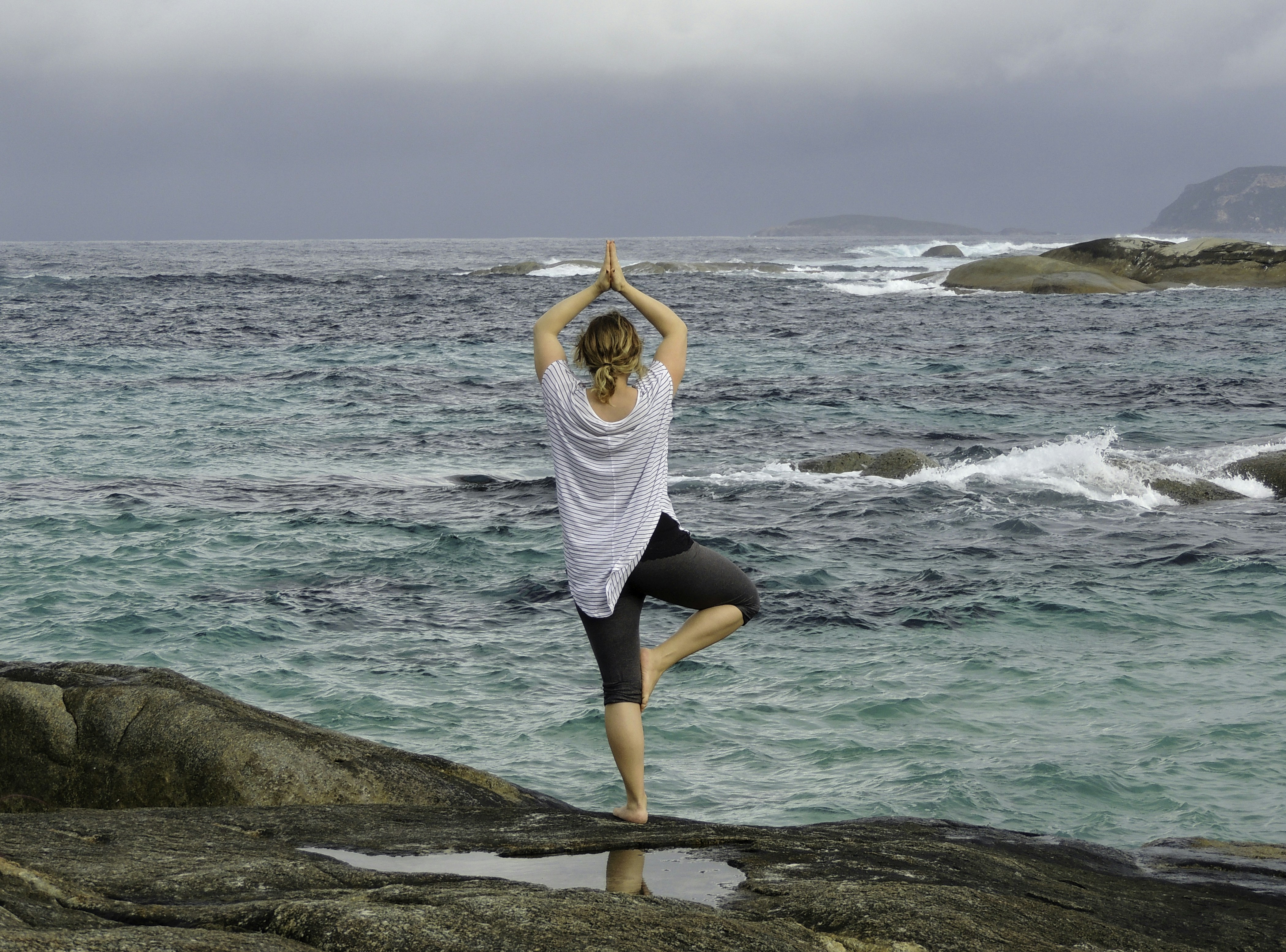 Tree Yoga Pose balancing on a rock overlooking expanse of Ocean with overcast skies in background. Finding balance through focus and contemplation of the massive expanse of the two toned sea.