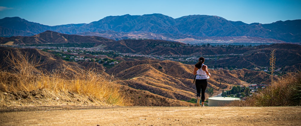 woman wearing white tank top walking on sand pathway