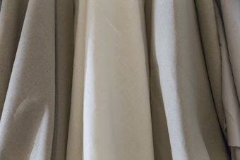 Several pieces of fabric hang side by side, showcasing a variety of textures and shades. The materials have a smooth appearance, with visible folds and creases that suggest they are draped or loosely hung.