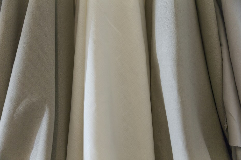 Several pieces of fabric hang side by side, showcasing a variety of textures and shades. The materials have a smooth appearance, with visible folds and creases that suggest they are draped or loosely hung.