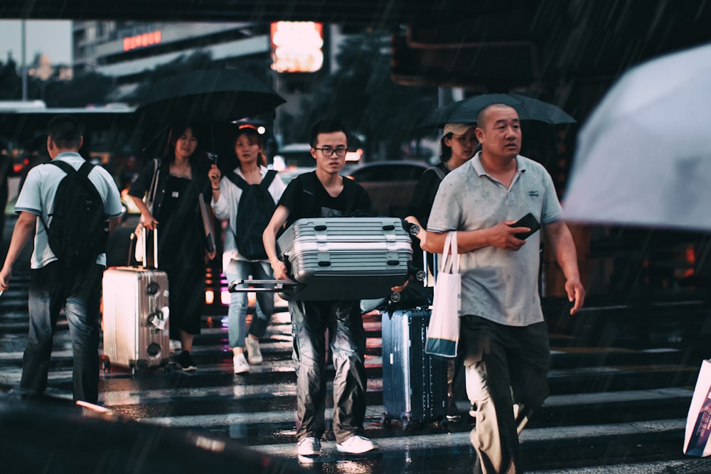 man wearing black polo shirt carrying gray travel luggage
