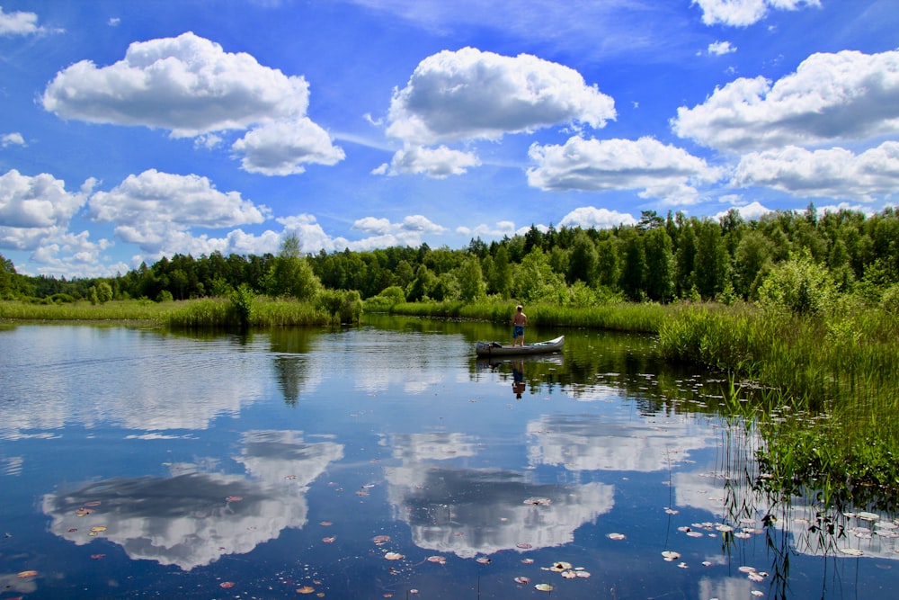 man on boat on body of water beside trees