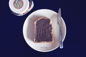 A rustic kitchen scene showing a slice of bread generously spread with lennat chocolate spread.