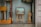 A shop window display contains a variety of handcrafted wooden items, including an easel with a framed picture, a standing wooden figure, and some other wooden objects. The word 'handicraft' is visible on a sign in the bottom left corner. The display conveys an artistic and artisanal vibe, with reflections on the glass slightly blurring the view.