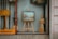 A shop window display contains a variety of handcrafted wooden items, including an easel with a framed picture, a standing wooden figure, and some other wooden objects. The word 'handicraft' is visible on a sign in the bottom left corner. The display conveys an artistic and artisanal vibe, with reflections on the glass slightly blurring the view.