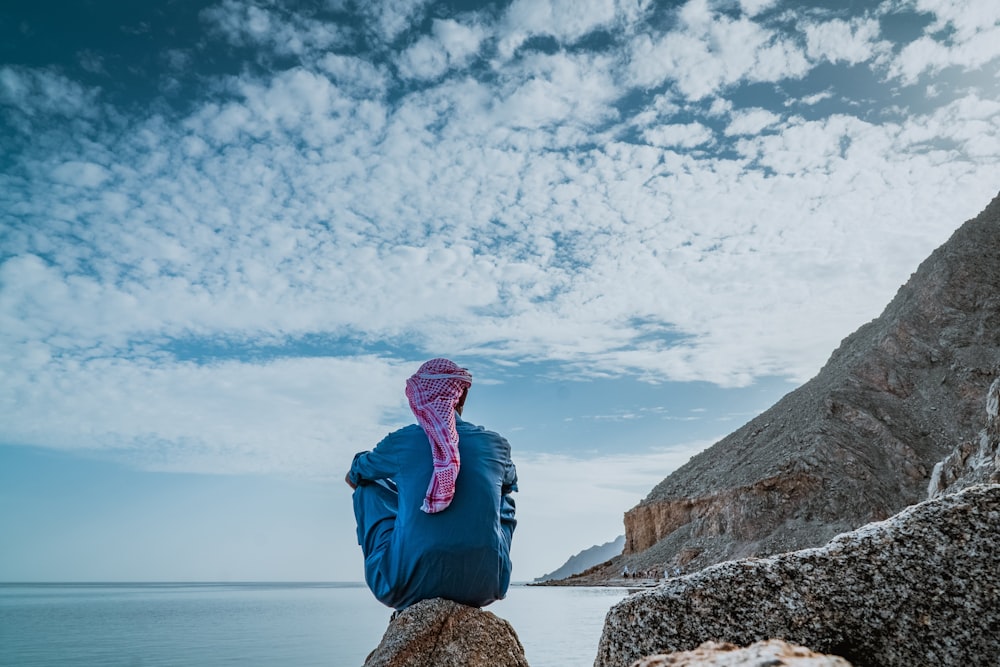 Mann in blaugrünem Thobe-Gewand sitzt auf Felsen