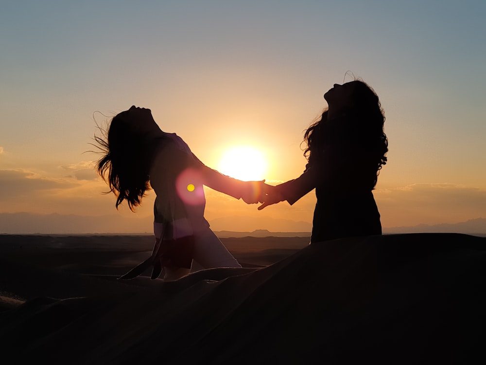 silhouette photo of two women holding each other hands