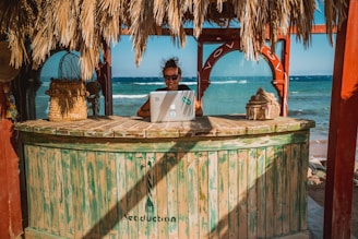 woman sitting on tiki bar facing silver laptop