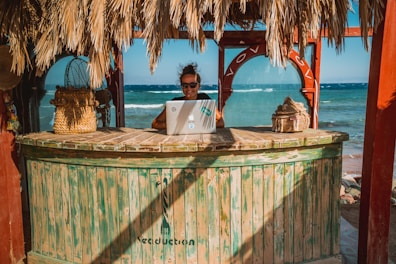 woman sitting on tiki bar facing silver laptop