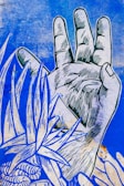 A stylized, graphic depiction of a hand with intricate line work. Surrounding the hand are abstract, organic shapes resembling leaves and a flower, all set against a textured blue background.