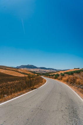 A winding road through the picturesque Italian countryside with a car driving towards the horizon under warm sunlight.