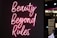 Neon pink script reads 'Beauty Beyond Rules' against a dark background with a partially visible sign in the background.