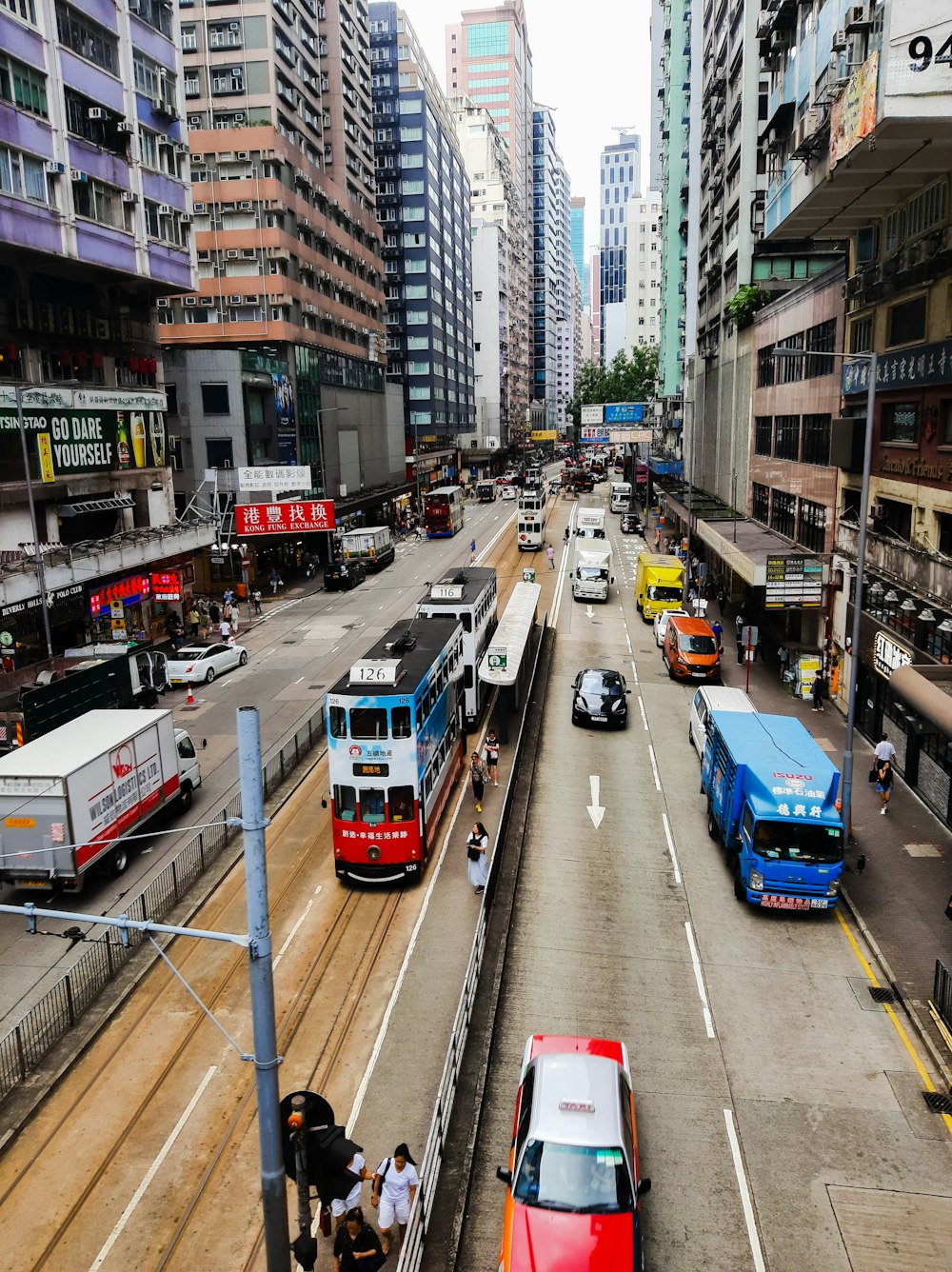 people walking on pathway near buildings and different vehicles on road during daytime