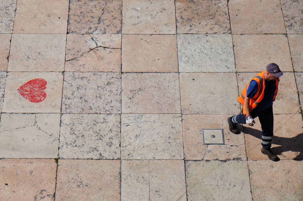 man wearing orange reflective vest walking on pathway during daytime