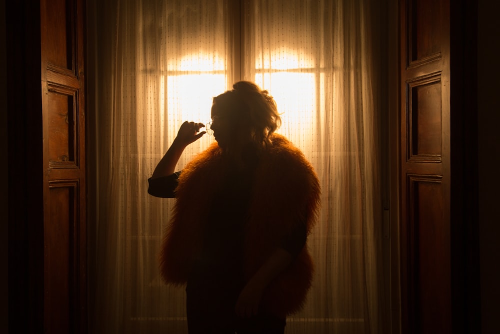 woman raising right hand while standing near curtain