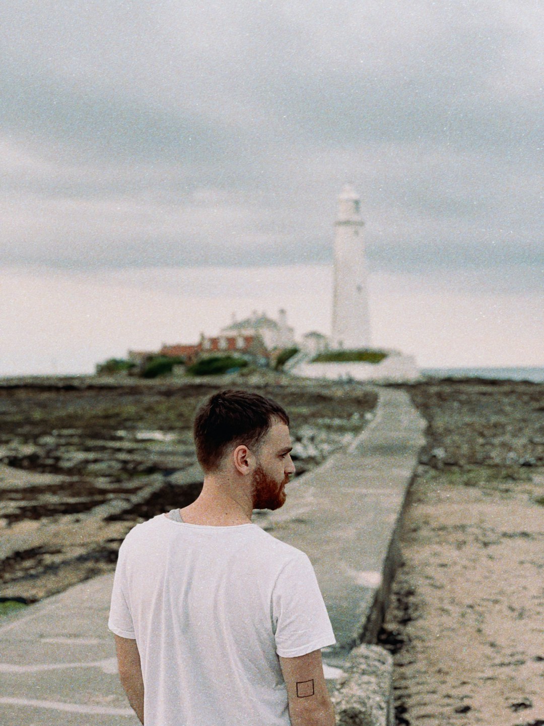 man standing on a concrete road leading to a lighthouse