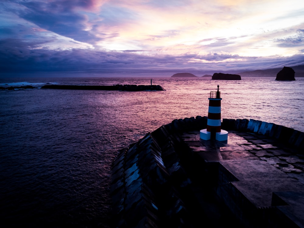 low-light photography of lighthouse near calm body of water