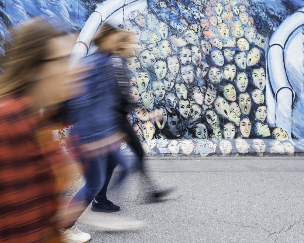 time lapse photography of three person walking beside graffiti wall