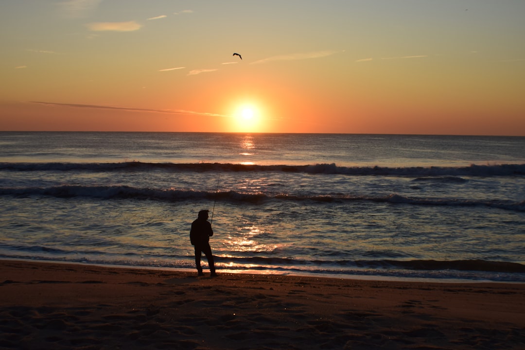 silhouette of person standing on seashore, Fishing from the beach at sunrise.