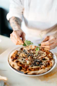 A chef sprinkling fresh herbs over a sizzling pizza in the kitchen of the Mexican pizzeria.