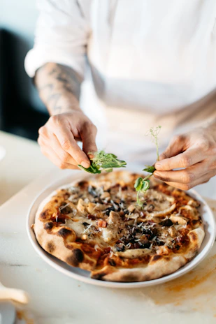 Chef carefully sprinkling herbs over a freshly made pizza with passion and precision.