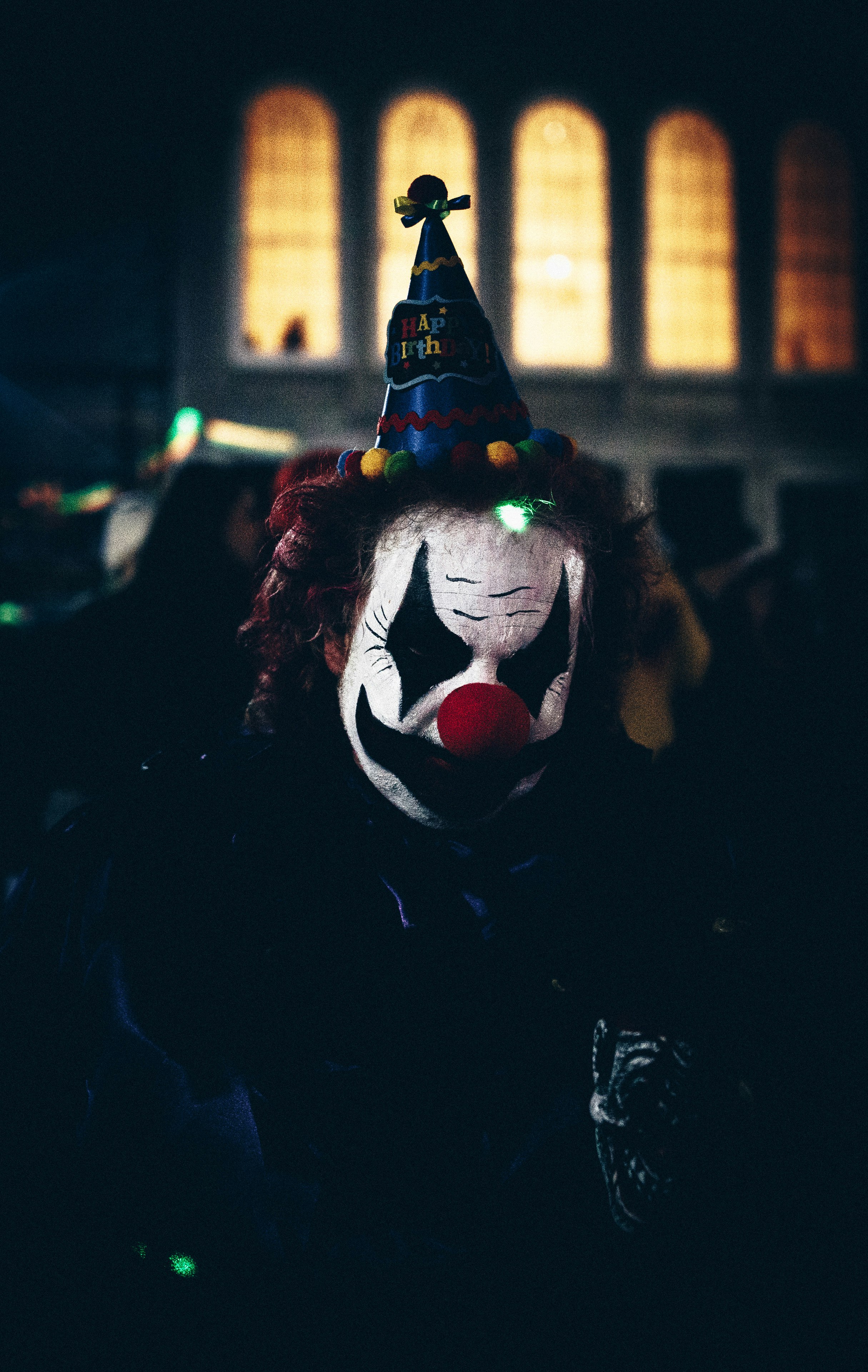person wearing multicolored cone party hat and clown mask