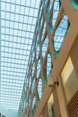 A modern architectural interior featuring a geometric design with large glass windows. The ceiling consists of a grid structure allowing natural light to illuminate the space. Walls display circles and diagonal lines, with a sleek and minimalistic design.