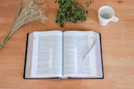 A journal and pen resting on a wooden table with scattered leaves around.