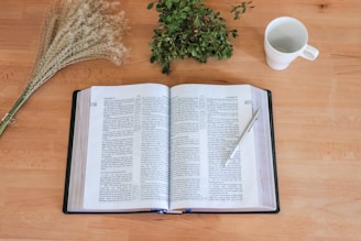 An open book of poetry placed on a rustic wooden table with a pen beside it.