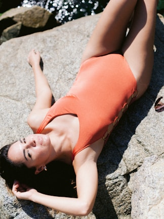 Model wearing a vibrant swimsuit sitting on a sunlit rock.