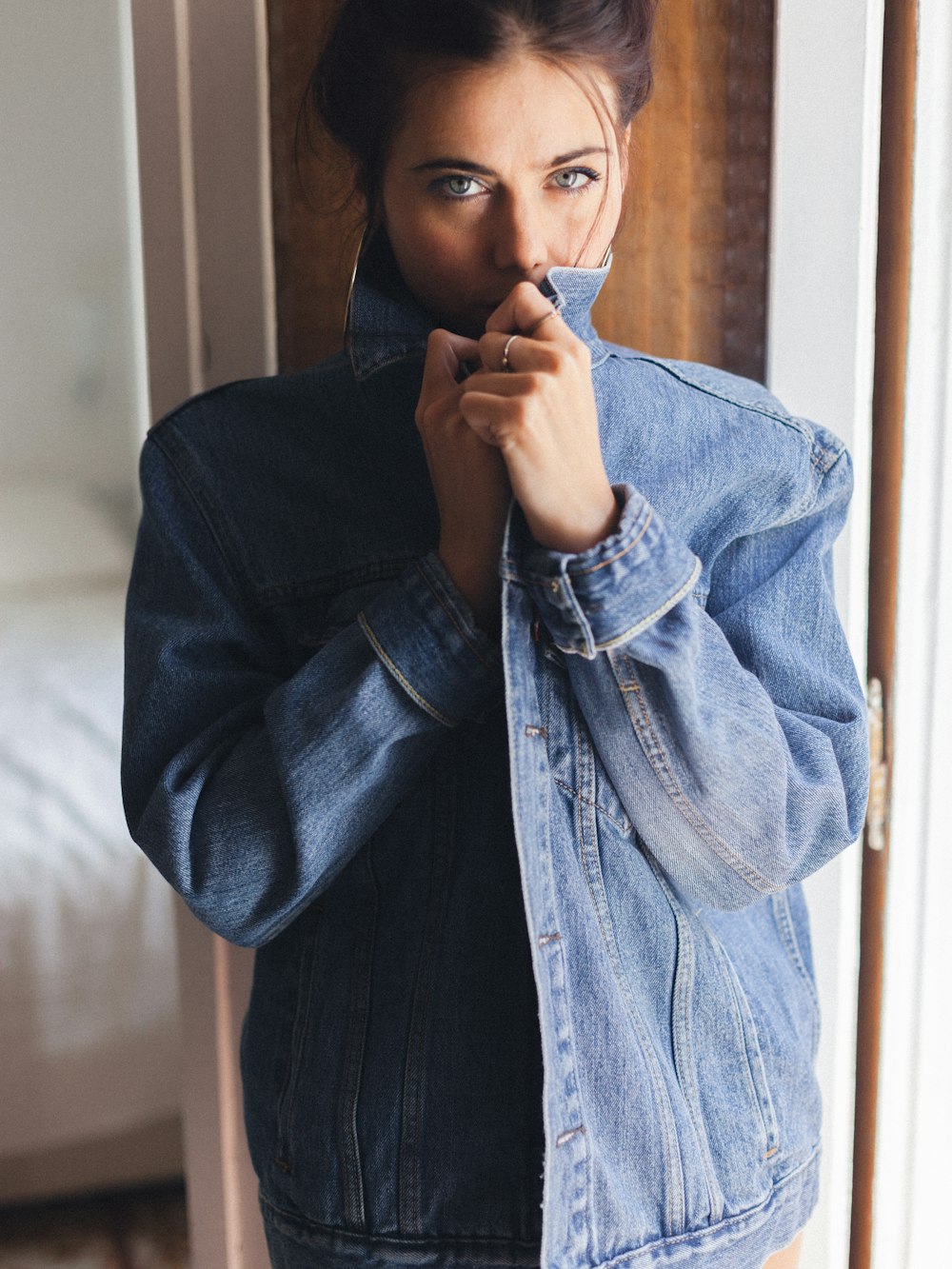 Femme en veste en jean bleue appuyée sur un mur en bois marron