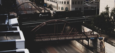 A light rail train crossing a bridge with city buildings in the background.