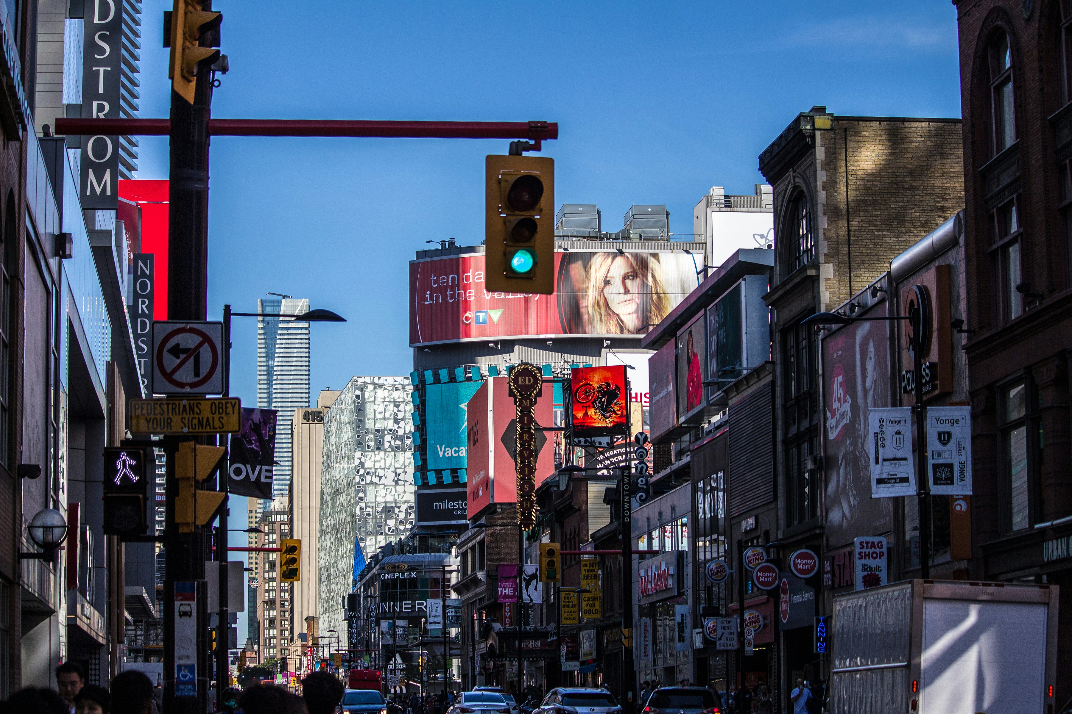 people walking on pathway near buildings and different vehicles on road under blue sky during daytime