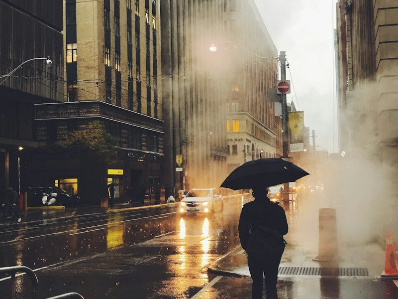 Persona con paraguas junto a una calle mojada durante la temporada de lluvias