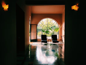 A cozy therapy room with two comfortable chairs, soft cream walls, and lush green plants by the window.