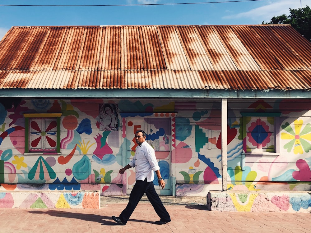 a man walking down a street past a colorful building
