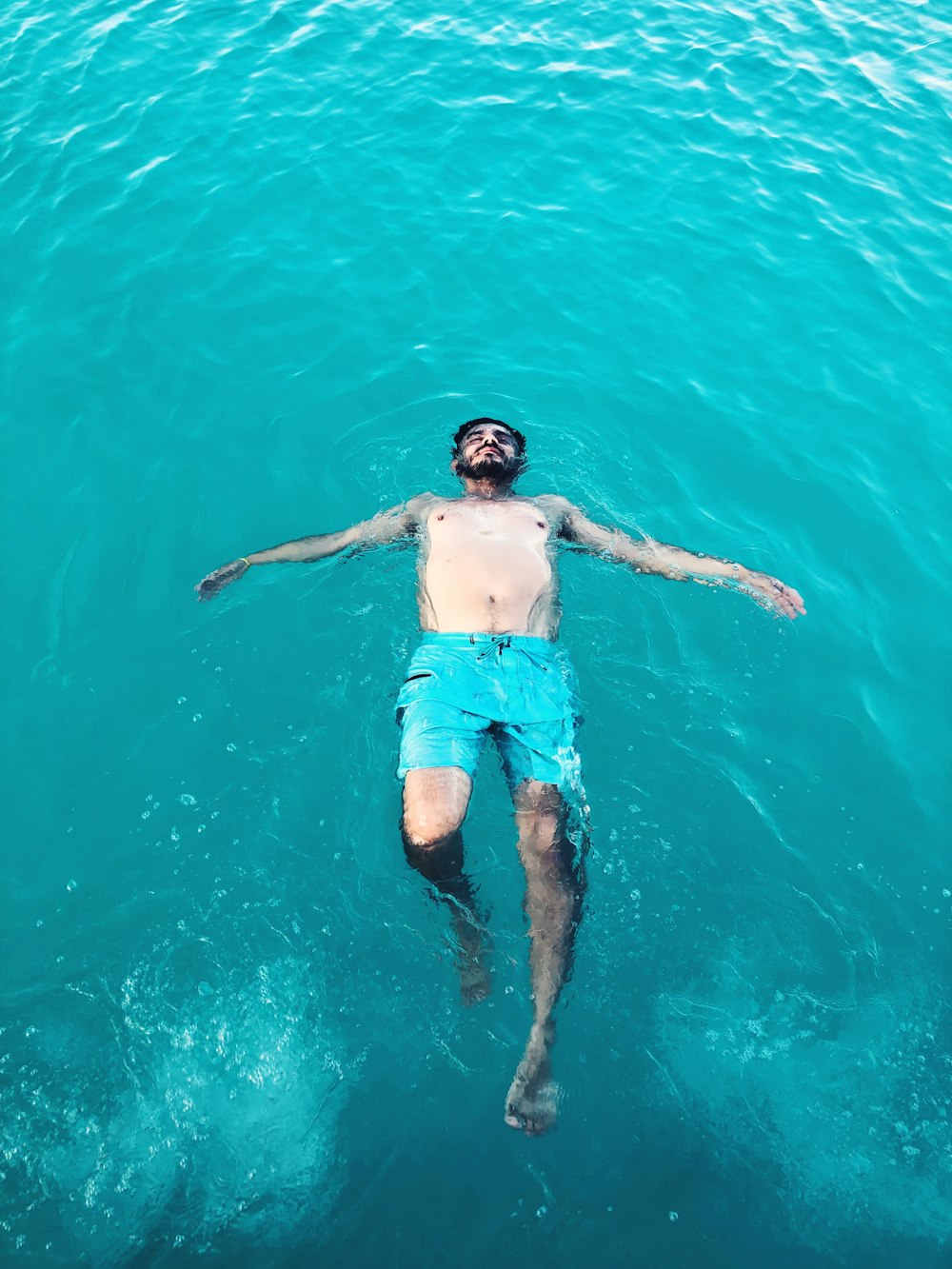 topless man swimming on body of water during daytime