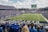 A large football stadium filled with fans watching a live game. Players are on the field, and the atmosphere is lively with a full audience. The scoreboard displays the action, and banners for the Kentucky Wildcats are visible.