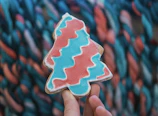 Hand holding a custom cookie cutter with a Guatemalan cultural design against a light pink backdrop.