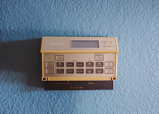 Close-up of a luxury thermostat set against a dark navy wall, glowing softly with ice blue accents.