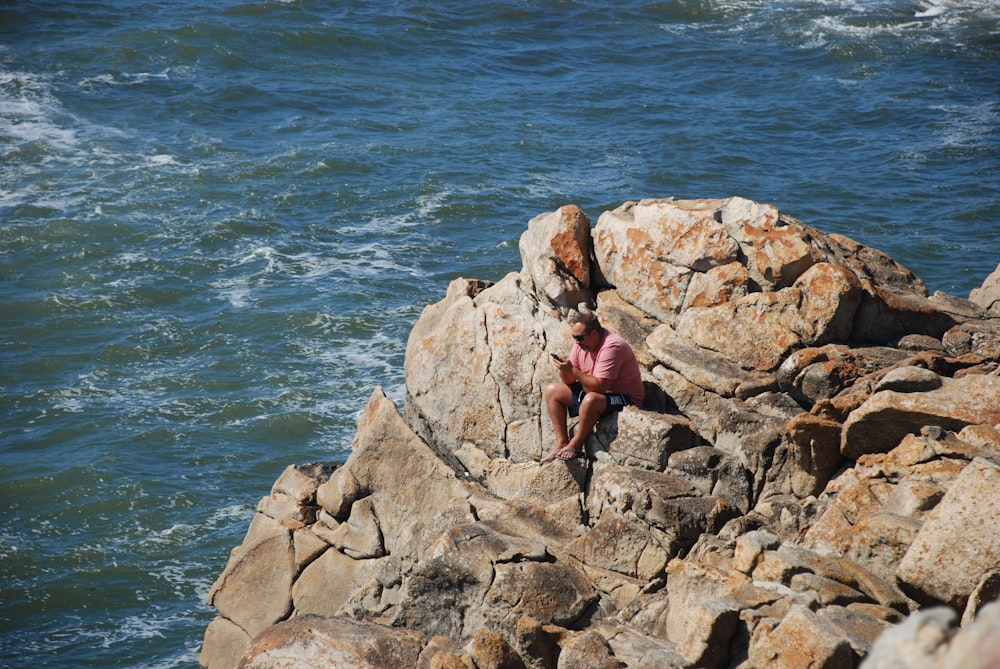man sitting on rock formation beside sae