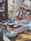 A fish market display features a variety of fresh seafood arranged on wooden tables. Baskets hold small fish, while large cuts of fish meat and whole fish are laid out neatly. The rustic setting includes tiled walls and weathered doors.