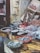 A fish market display features a variety of fresh seafood arranged on wooden tables. Baskets hold small fish, while large cuts of fish meat and whole fish are laid out neatly. The rustic setting includes tiled walls and weathered doors.