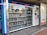 A vending machine filled with neatly arranged books is situated outdoors. There is a digital display above the machine showing text in a language that appears to be Chinese. Next to the machine is a panel with information and instructions, possibly related to how to operate it.