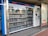 A vending machine filled with neatly arranged books is situated outdoors. There is a digital display above the machine showing text in a language that appears to be Chinese. Next to the machine is a panel with information and instructions, possibly related to how to operate it.