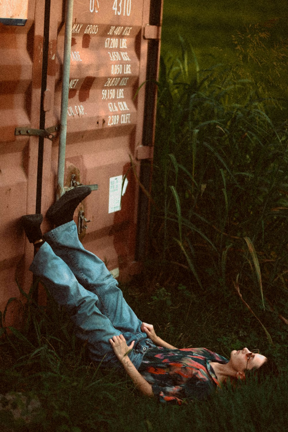 man lying on grass beside intermodal container