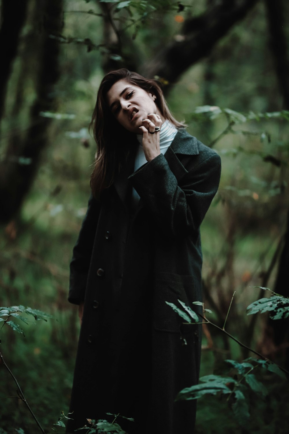 standing woman in black coat surrounded by plants
